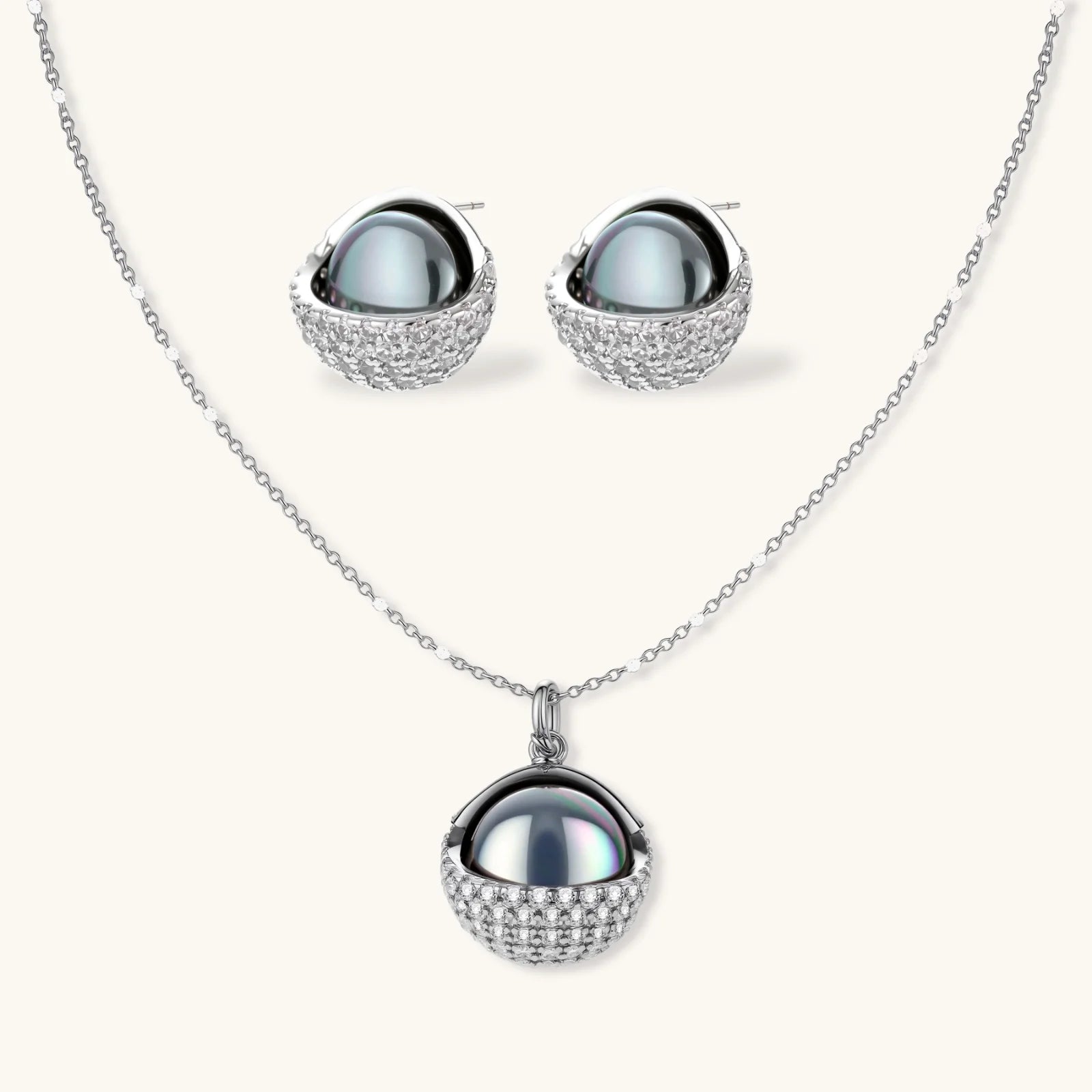 Elegant spherical pendant necklace and earrings set featuring crystal-pavé bottom half in gold or silver finish on white background.